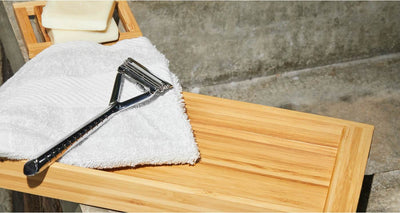 A chrome razor sits on a white towel on top of a bamboo shelf.