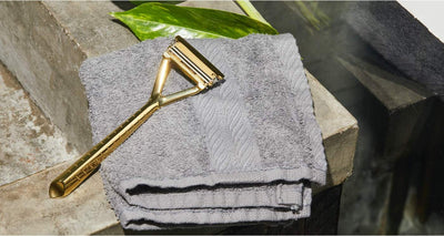 A gold razor sits on a grey towel on top of a bathroom counter.