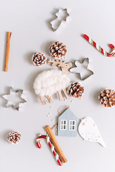 A flat lay image of a wooden sheep, cookie cutters, candy canes and pinecones. 