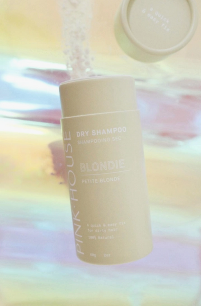 Photo of a compostable beige container with white text which contains natural dry shampoo. The background is a blend of pastel colours.