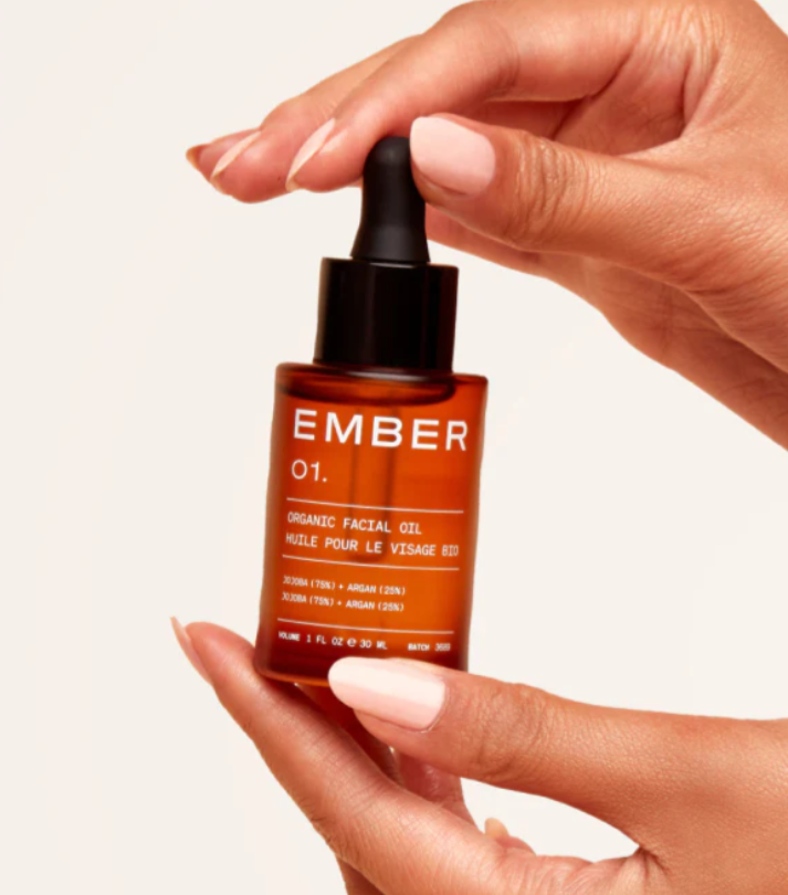 A pair of hands holding a 12ml amber bottle of facial oil with a dropper top. 