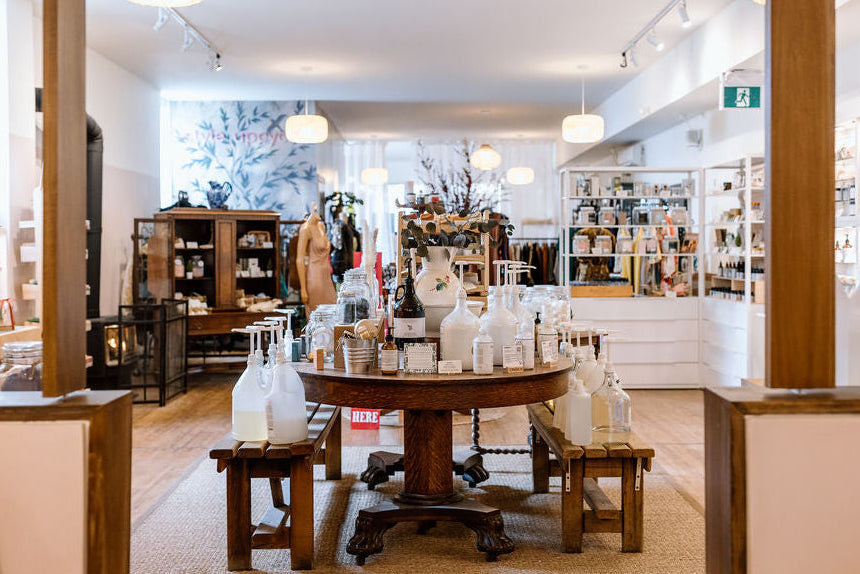 Store interior with wooden table and decorative bottles, surrounded by shelves and displays.