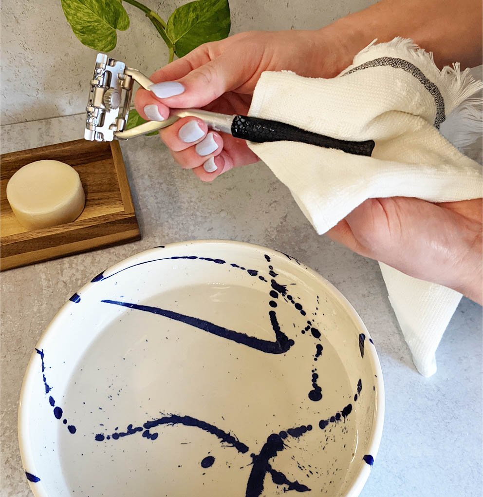 One hand holds the top of the razor while the handle is covered in a towel with another hand.