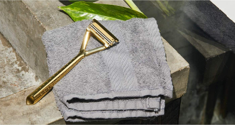 A gold razor sits on a grey towel on top of a bathroom counter.