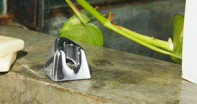 A chrome razor stand sits on a counter with a plant in the background